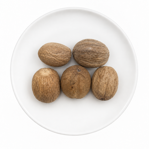 Nutmeg, whole dry product on a plain white plate against a white background
