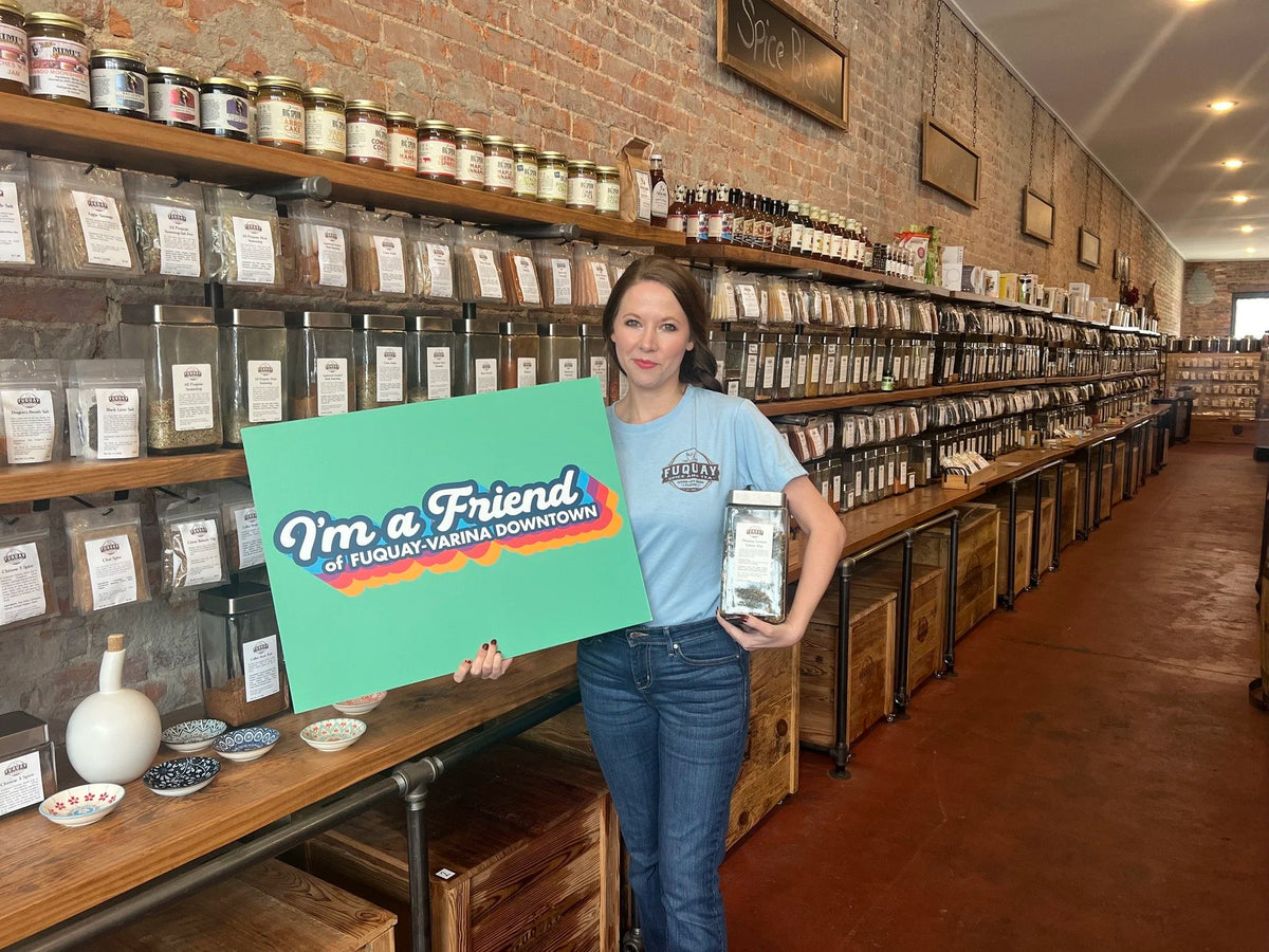 A customer inside Fuquay Spice & Tea holding a Friend of Fuquay-Varina Downtown sign.