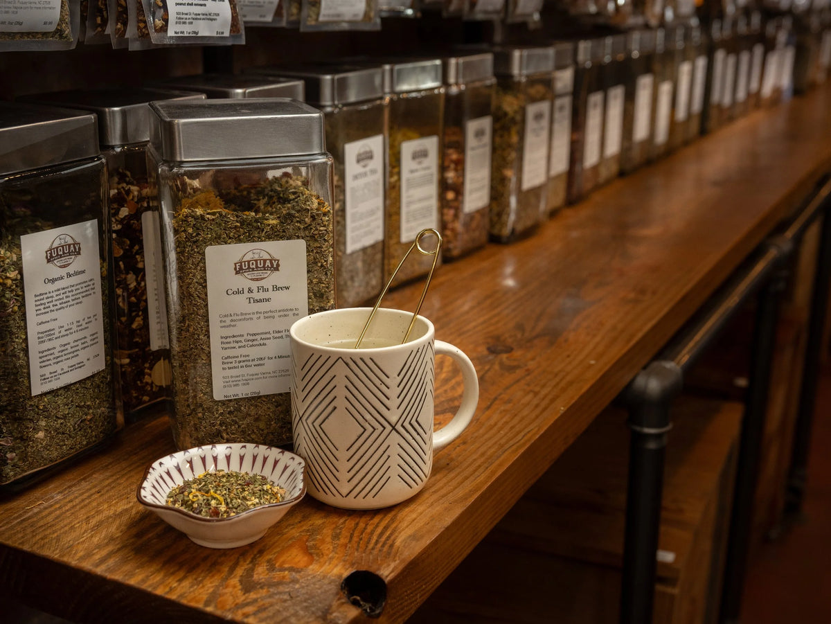 Glass jars of herbs and tea displayed on a wooden shelf with a cup of tea.
